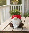 Gnome planter with a white beard, brown boots, and red hat sitting on a wooden table outdoors.